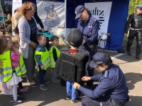 Dwie policjantki ubierają małego chłopca w sprzęt PZ, obok stoi kilkoro dzieci z nauczycielką.