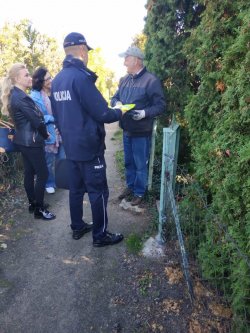 policjant stoi na ścieżce i rozmawia z napotkanymi osobami o zabezpieczeniu ogródków działkowych