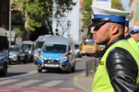 policjant stojący przy drodze, w oddali radiowóz policyjny