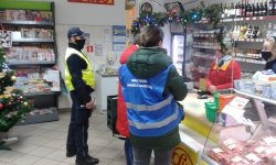 pracownicy inspekcji i policjant stoją w sklepie i rozmawiają z dwiema pracownicami sklepu stojącymi za ladą.