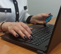 kobieta siedząca przy komputerze i trzymająca w ręku kartę bankomatową
