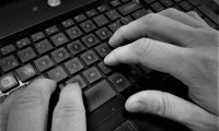 czarno białe zdjęcie klawiatury komputera, na której widać dłonie osoby piszącej tekst