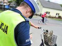 Na obrazku widzimy policjanta Ruchu Drogowego piszącego w notatniku a w oddali widzimy rowerzystów.